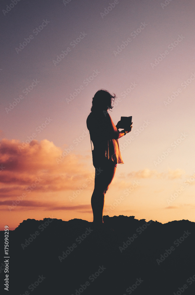 Anonymous, unrecognizable silhouetted female taking a photo of a beautiful sunset with smartphone