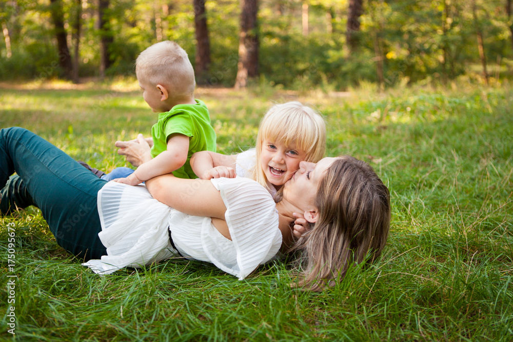 © justesfir - Family concept, mother playing with her kids and kissing her daughter on the grass © justesfir - Family concept, mother playing with her kids and kissing her daughter on the grass