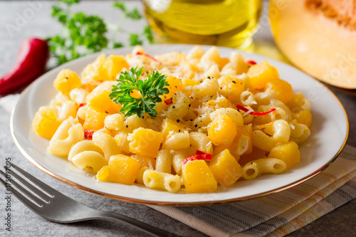 Pasta with pumpkin, chili and cheese in plate on stone background