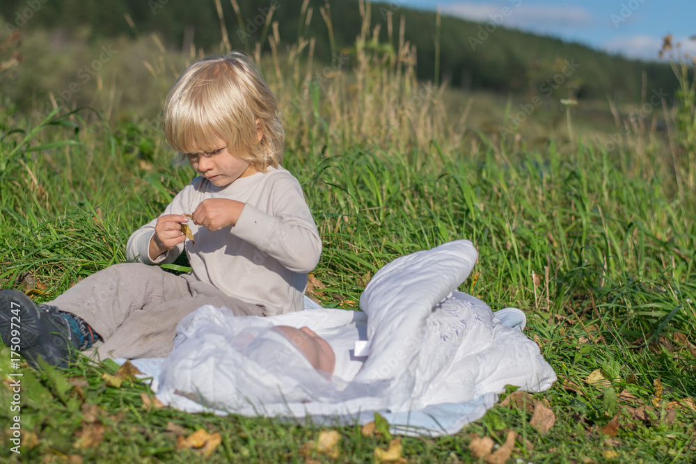 A blond boy with younger newborn brother siiting on a grass during outing
