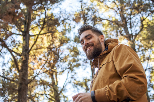Low angle portrait of a handsome caucasian man with a beard very smiling and behind nature in autumn.