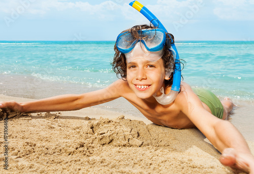 Cute kid in scuba mask laying on sandy beach