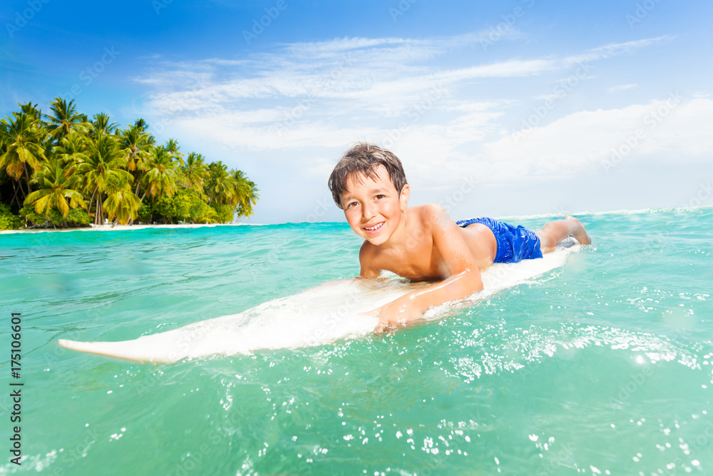 Happy little boy swim on surfing board in the sea