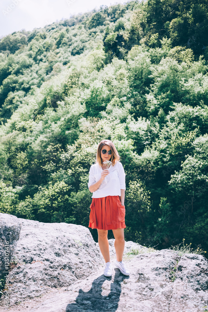 Naklejka premium Young woman on the rock in nature with flowers in her hands