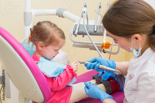Little girl sitts in dental chair at dentist office talking with female doctor