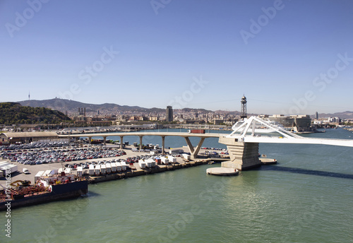 Aerial view of Barcelona port. Big cruise ship is waiting to depart. Many cars and containers to be shipped. Modern bridge and the city are in the view. © theendup