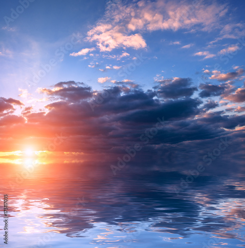 The blue sky above the storm clouds at sunset over calm water.