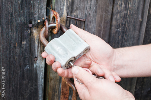 Dirty hand of man with key unlocking the padlock on the wood door of the hangar photo