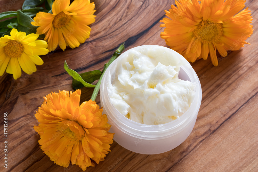 A jar of calendula cream, with calendula flowers in the background A jar of calendula cream, with calendula flowers in the background
