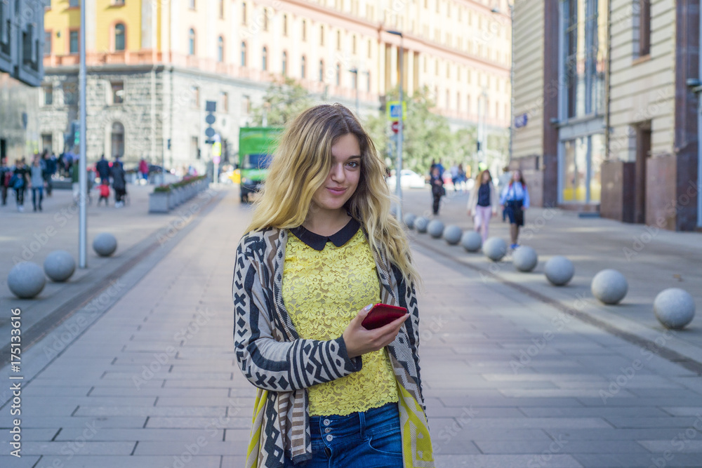 Young beautiful pretty girl walking along the street with phone in hand