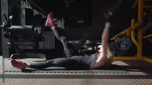 Fitness woman doing crunch exercise to the raised leg on the mat in the gym