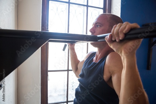Male athlete practicing pull ups on bar by window