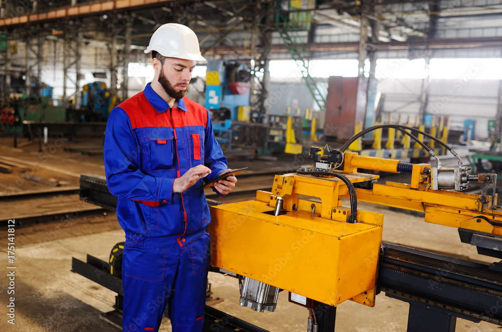 Man working in a construction helmet with a tablet on the background of a plant Man working in a construction helmet with a tablet on the background of a plant