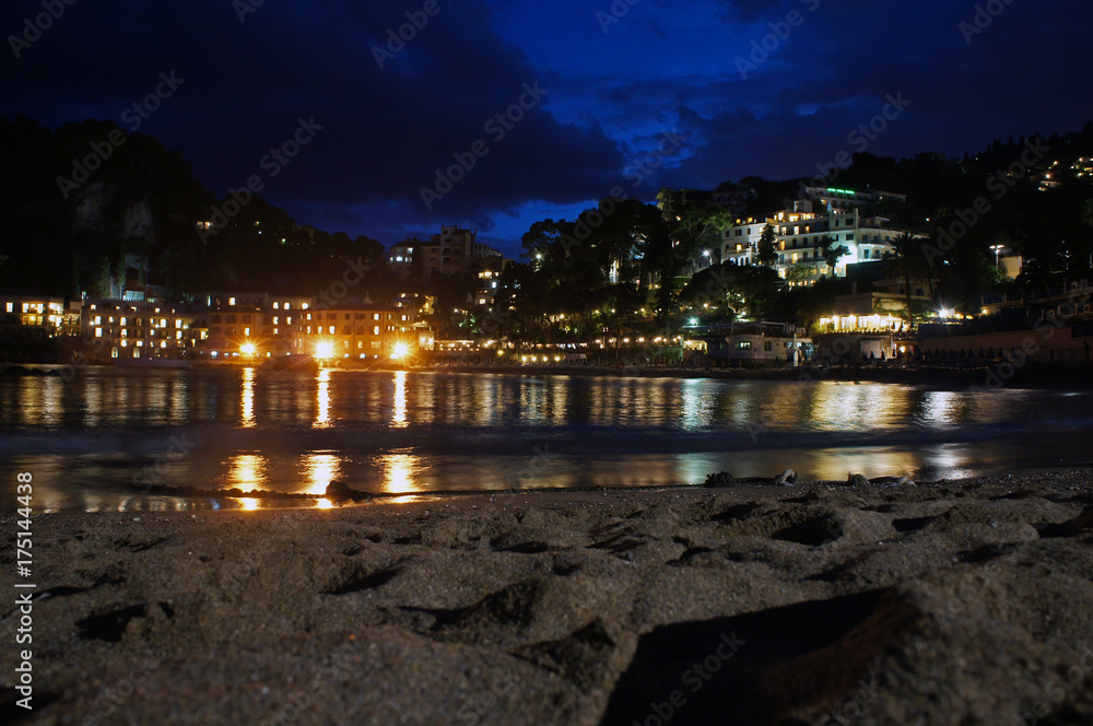 Night panorama of Taormina and the boat on the sandy beach bay