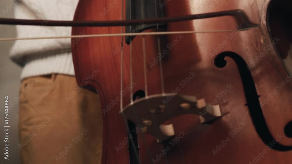 Young caucasian bearded man with mohawk and ear pearcing in white knitted pullover playing contrabass with fiddlestick Young caucasian bearded man with mohawk and ear pearcing in white knitted pullover playing contrabass with fiddlestick