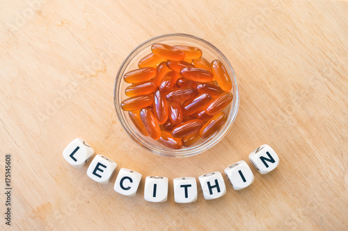 Lecithin gel pills in a round glass bowl and with the word Lecetin from the letters of cubes on a light wooden background. Soy and sunflower lecithin benefits for skin, digestion, lower cholesterol. photo