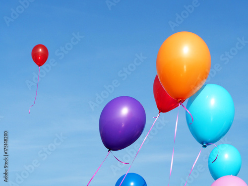 Multicolored inflatable balloons filled with helium against the blue sky, one red balloon flew away