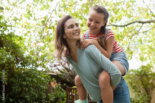 Принти на полотні Cheerful mother giving daughter piggyback ride against trees