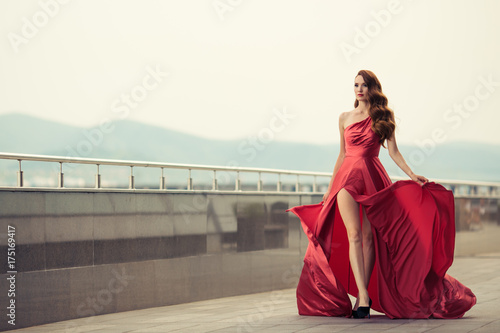Beautiful woman in red fluttering dress. Urban background.