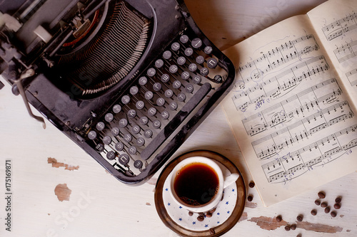 Old metal typewriter, covered in dust and rust. Cup of coffee on the table. The atmosphere of comfort and creativity. Retro