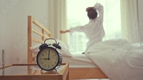 Closeup alarm clock, Young asian woman wake up in the morning and sitting on bed at mirror door side relaxing in holiday with sunlight, Vintage 