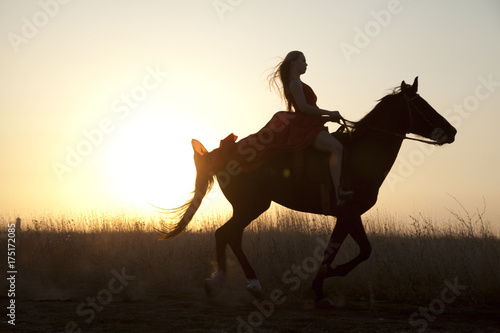 Young woman in a long dress riding on horse at sunset