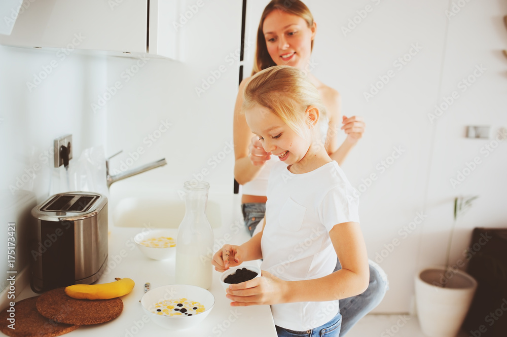 mother having breakfast with kid daughter at home in modern white kitchen, cozy lifestyle in the morning