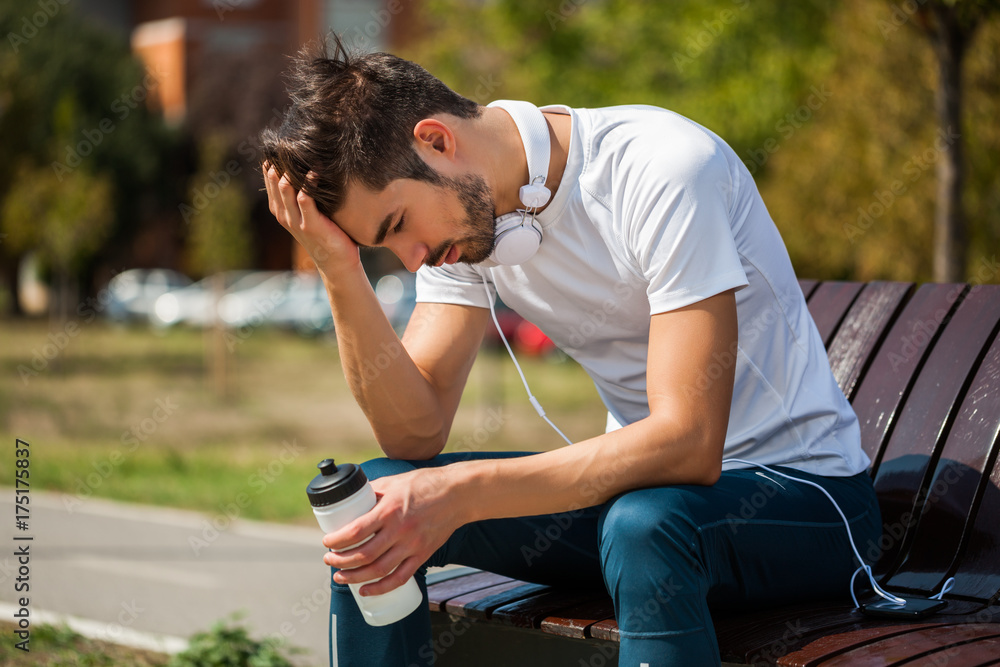 Young man is relaxing and drinking water after jogging. 