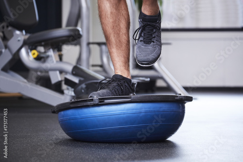 Dude jogging on bosu ball in gym, close up
