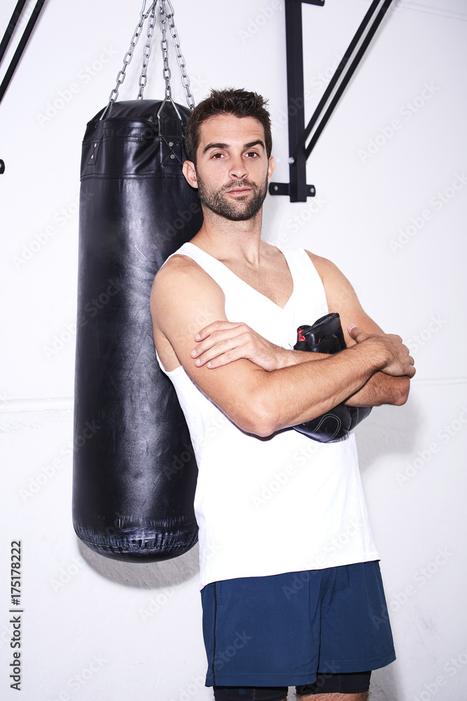Boxer leaning against punch bag in gym, portrait