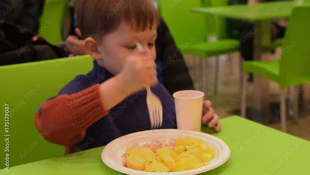 Little boy eating potatoes with meat in food court of shopping centre Little boy eating potatoes with meat in food court of shopping centre