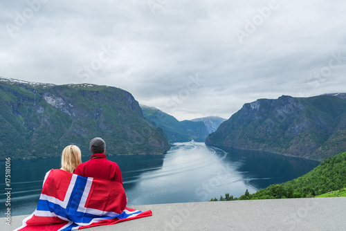 Couple with the flag of Norway looks at the fjord