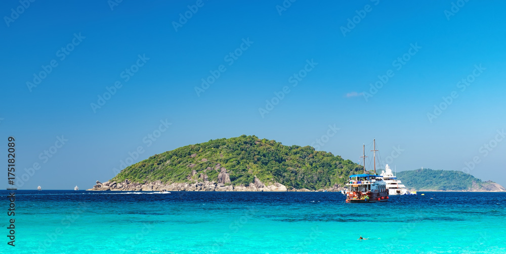 Obraz premium View from the beach to the crystal blue water of the Andaman Sea and Similan Island, Thailand. Tourist boats and the island on the horizon, sea cruise in tropical waters
