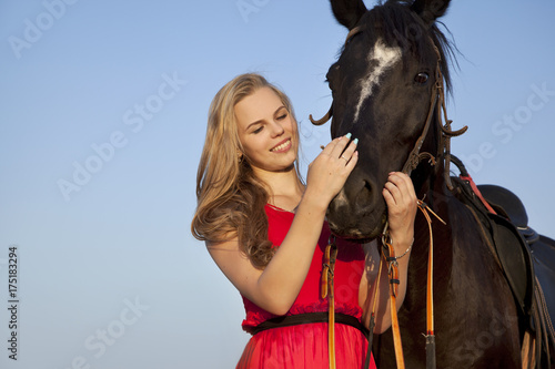 Smiling blonde stroking a horse. Portrait of a young woman with a stallion