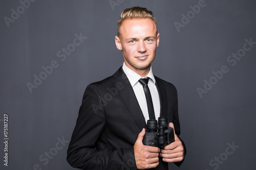 Businessman in suit looking through binoculars in hands with gray background photo