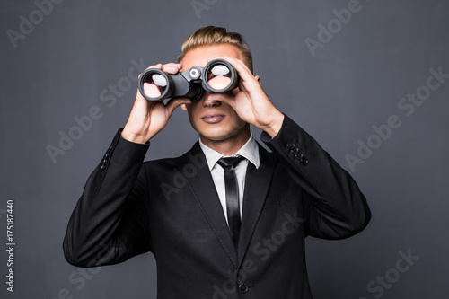 Handsome young american businessman using binoculars in office on gray background