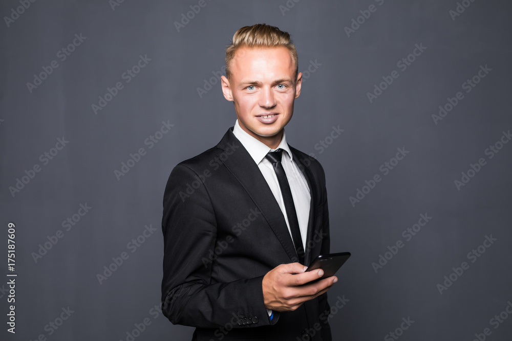 Happy business man in black suit typing sms on smartphone on grey Happy business man in black suit typing sms on smartphone on grey