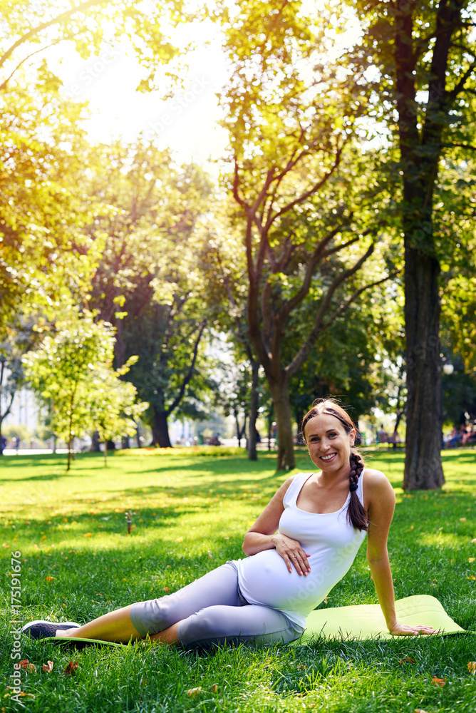 Relaxed pregnant woman sitting on yoga mat in park Relaxed pregnant woman sitting on yoga mat in park