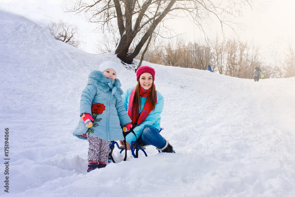 A young mother walks with her daughter in the snow and sits on a sled A young mother walks with her daughter in the snow and sits on a sled
