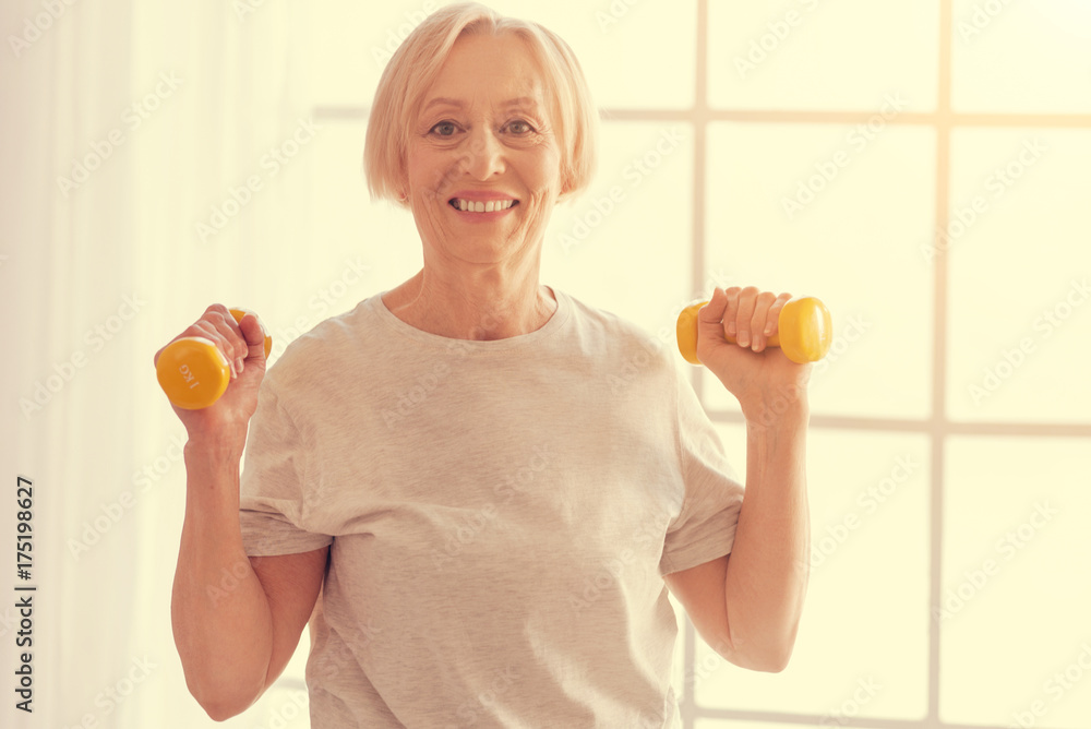 Positive senior woman exercising with dumbbells at home Positive senior woman exercising with dumbbells at home