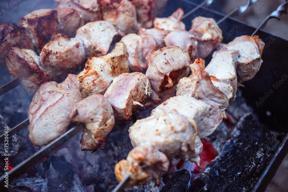 Grilled kebab cooking on metal skewers (grill). Roasted meat cooked at barbecue with smoke. Close up BBQ fresh pork meat chop slices. Traditional eastern dish, shish kebab. Grilled kebab cooking on metal skewers (grill). Roasted meat cooked at barbecue with smoke. Close up BBQ fresh pork meat chop slices. Traditional eastern dish, shish kebab.