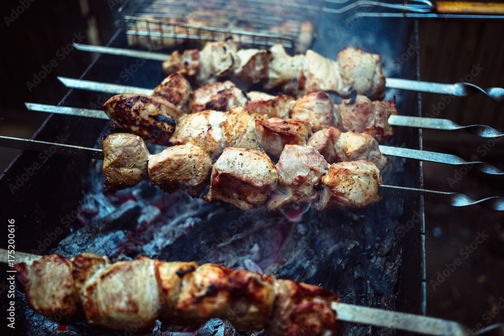 Grilled kebab cooking on metal skewers (grill). Roasted meat cooked at barbecue with smoke. Close up BBQ fresh pork meat chop slices. Traditional eastern dish, shish kebab. Grilled kebab cooking on metal skewers (grill). Roasted meat cooked at barbecue with smoke. Close up BBQ fresh pork meat chop slices. Traditional eastern dish, shish kebab.