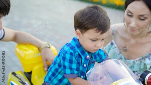 Young parents watching little boy riding toy car at street. Happy parents spending time with little son helping him to ride new play car at street. photo