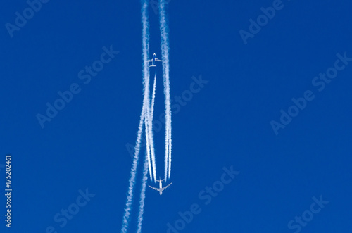 Airplane crosses the contrail of another aircraft against the blue sky.