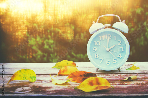 Image of autumn Time Change. Fall back concept. Dry leaves and vintage alarm Clock photo