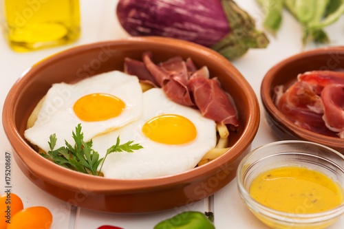 Fried eggs in a ceramic cup with spanish jamon for breakfast on a white background
