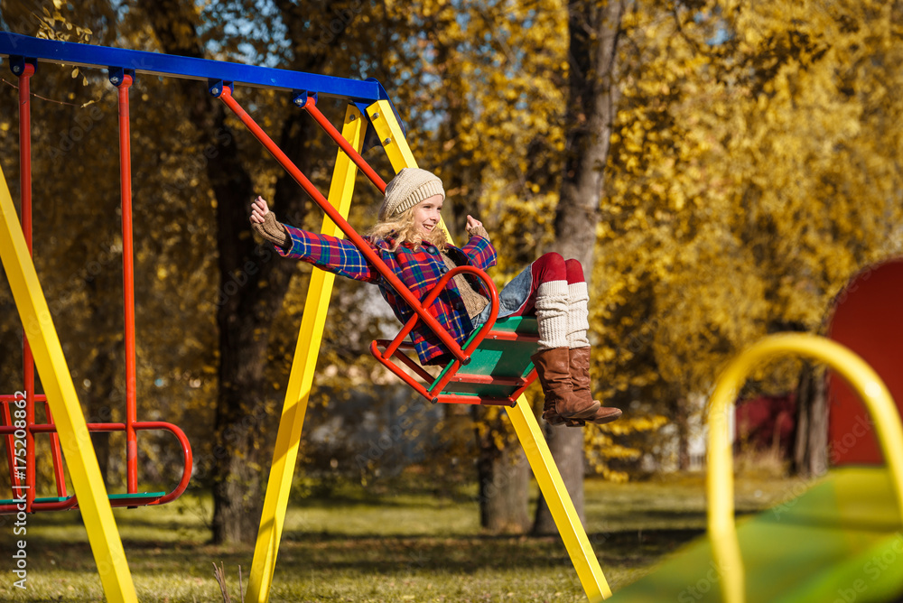 A young girl in coat is riding on a swing at playground. Autumn park