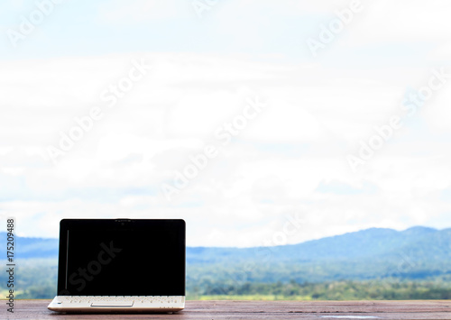 Laptop stands on a wooden table outdoors and nature background