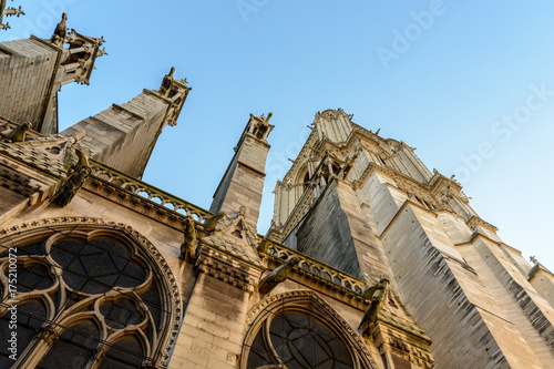 View from below of the North tower of Notre-Dame de Paris cathedral at sunset with buttresses and gargoyles.