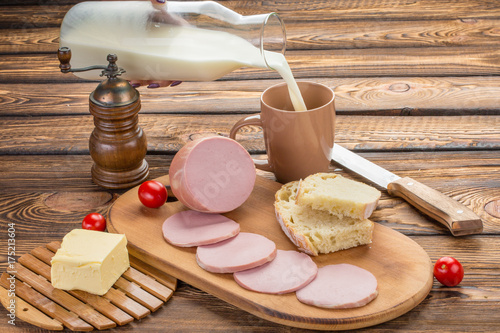 still life of Sliced boiled sausage with ingredients. rural breakfast - boiled sausage, bread, milk, butter, tomatoes over wooden background photo